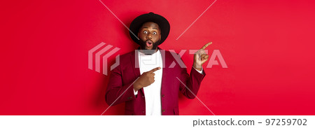 Winter holidays and shopping concept. Happy Black man pointing left and smiling, showing new year promo offer on red background 97259702