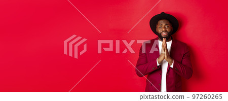 Miserable Black man asking for help, begging for favour and looking sad, standing against red background 97260265