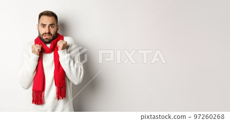Christmas holidays and celebration concept. Scared man trembling from fear and looking startled, standing anxious in red scarf and white sweater 97260268