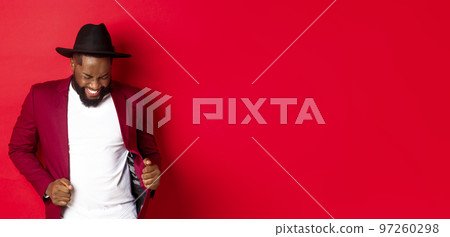 Christmas and people concept. Happy Black man celebrating New Year and dancing, wearing party outfit, red background 97260298