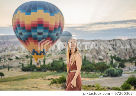 Tourist woman looking at hot air balloons in Cappadocia, Turkey. Happy Travel in Turkey concept. Woman on a mountain top enjoying wonderful view 97260362