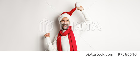 Winter holidays and New Year party concept. Happy man celebrating Christmas dancing in Santa hat and red scarf, standing against white background Winter holidays and New Year party concept. Happy man celebrating Christmas dancing in Santa hat and red scarf, standing against white background 97260586