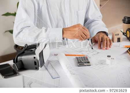 Architect workplace. Architectural building design and construction plans with blueprints paper project plans and VR glasses, designing man edit a building or architecture drawing with compass divider Architect workplace. Architectural building design and construction plans with blueprints paper project plans and VR glasses, designing man edit a building or architecture drawing with compass divider 97261629