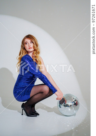 woman in shiny blue dress on floor with a disco ball on a white room woman in shiny blue dress on floor with a disco ball on a white room 97261671