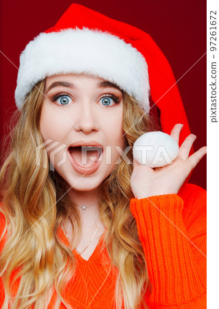 a surprised beautiful woman in a Santa Claus hat on a red background. a surprised beautiful woman in a Santa Claus hat on a red background. 97261672