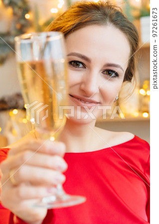 close up. a woman in a red with a glass of champagne in a room with garlands. close up. a woman in a red with a glass of champagne in a room with garlands. 97261673