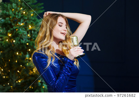 a beautiful woman in a shiny dress with a retro microphone at the Christmas tree 97261682