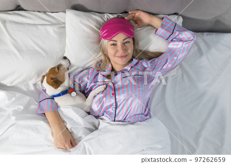 An attractive young woman wearing pajamas is holding a dog while laying on a bed 97262659