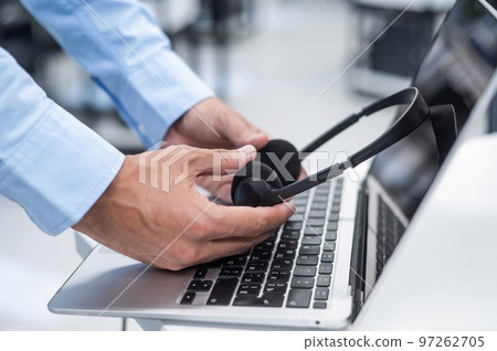 A man puts a headset on a laptop keyboard in the office. A man puts a headset on a laptop keyboard in the office. 97262705
