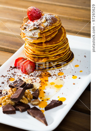 Stack of sweet pancakes with fruit, honey, chocolate and whipped cream 97265629