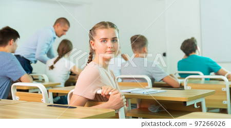Positive teenage schoolgirl sitting at lesson in classroom 97266026