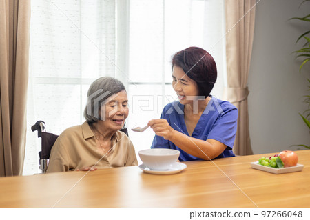 Caregiver feeding elderly asian woman with soup. Caregiver feeding elderly asian woman with soup. 97266048