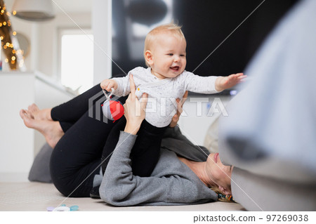 Happy family moments. Mother lying comfortably on children's mat playing with her baby boy watching and suppervising his first steps. Positive human emotions, feelings, joy 97269038