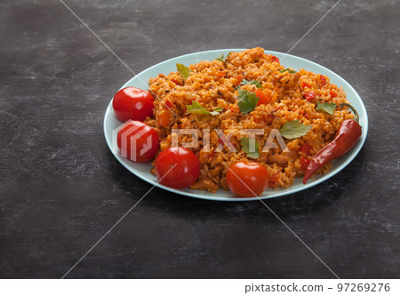 Jollof rice, tomatoes and hot peppers on a blue plate on a black background. National cuisine of Africa. Jollof rice, tomatoes and hot peppers on a blue plate on a black background. National cuisine of Africa. 97269276