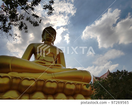 Golden big Buddha statue in Wat Pak Nam Phasi Charoen temple. Sunlight sky and cloud background 97269565