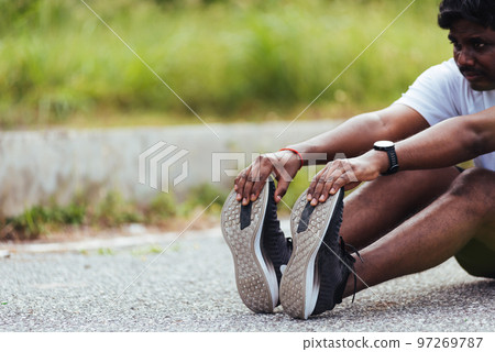 Close up Asian young athlete sport runner black man wear watch he sitting pull toe feet stretching legs and knee before running at outdoor street health park, healthy exercise before workout concept Close up Asian young athlete sport runner black man wear watch he sitting pull toe feet stretching legs and knee before running at outdoor street health park, healthy exercise before workout concept 97269787