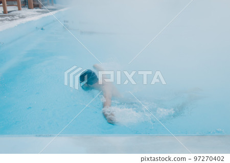 Fit swimmer male training swim in open winter swimming pool with fog. Geothermal outdoor spa health concept. 97270402