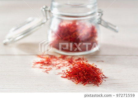 Dried saffron spices in a glass storage jar, on a wooden table. 97271559