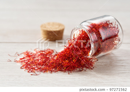 Dry saffron threads in a glass jar scattered on a white table. 97271562