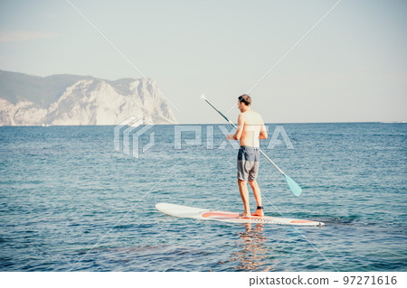 Side view foto of a man swiming and relaxing on the sup board. Sportive man in the sea on the Stand Up Paddle Board SUP. The concept of an active and healthy life in harmony with nature. Side view foto of a man swiming and relaxing on the sup board. Sportive man in the sea on the Stand Up Paddle Board SUP. The concept of an active and healthy life in harmony with nature. 97271616