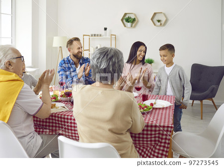 Big family congratulates child boy and clapping hands during family dinner in living room. Big family congratulates child boy and clapping hands during family dinner in living room. 97273545