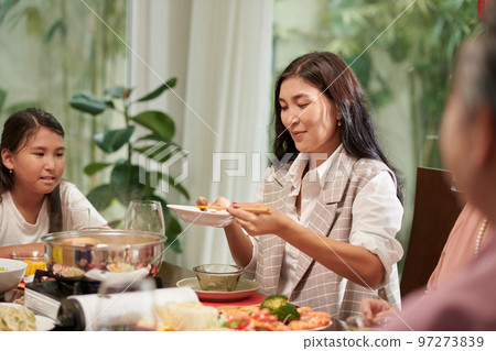 Smiling mature woman filling her plate at family dinner Smiling mature woman filling her plate at family dinner 97273839