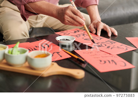 Hands of eldelry man painting on red paper when creating greeting cards for Tet Hands of eldelry man painting on red paper when creating greeting cards for Tet 97273883