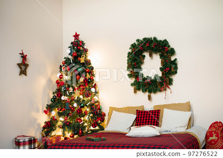 Cozy Decorated bedroom for Christmas holidays with tree. Spacious white light bedroom with a decorated Christmas spruces, garland, bed with pillows. interior xmas bedroom Cozy Decorated bedroom for Christmas holidays with tree. Spacious white light bedroom with a decorated Christmas spruces, garland, bed with pillows. interior xmas bedroom 97276522