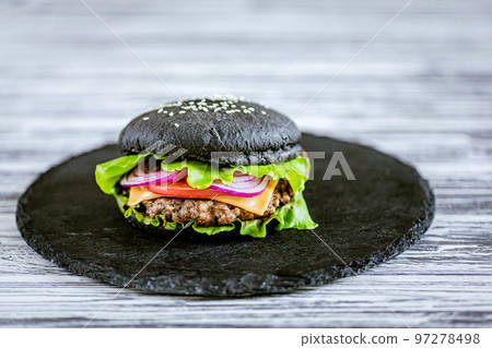 Front view of appetit black burger with meat cutlet and vegetables on black stone board. Free Space Front view of appetit black burger with meat cutlet and vegetables on black stone board. Free Space 97278498