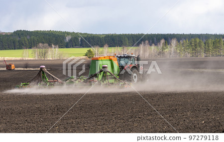 Spring field work, a tractor with a trailed seeder sows seeds in an agricultural field Spring field work, a tractor with a trailed seeder sows seeds in an agricultural field 97279118