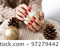 Female hands with red manicure and gold foil on the nails. Winter and Christmas time concept. Manicured woman's hands with Christmas decoration. 97279442