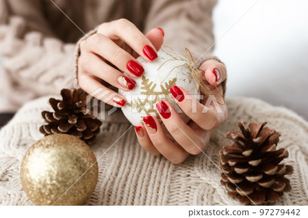 Female hands with red manicure and gold foil on the nails. Winter and Christmas time concept. Manicured woman's hands with Christmas decoration. Female hands with red manicure and gold foil on the nails. Winter and Christmas time concept. Manicured woman's hands with Christmas decoration. 97279442