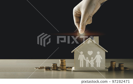 Hand putting a glowing coin on the model home bank with a pile of coins. The concept for the management of financial home loans or money saving for house buying. Hand putting a glowing coin on the model home bank with a pile of coins. The concept for the management of financial home loans or money saving for house buying. 97282471