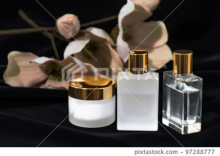 3 glass cosmetic containers with gold lids arranged in a floral background 97288777