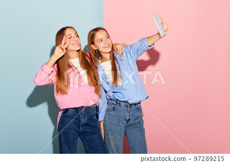 Beautiful and happy teen girls, sisters or friends taking picture isolated over colorful background. Fashion, beauty, emotions, friendship and ad 97289215