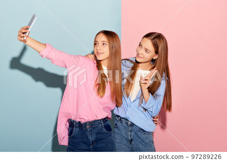 Beautiful and happy teen girls, sisters or friends taking picture isolated over colorful background. Fashion, beauty, emotions, friendship and ad 97289226