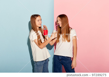 Party. Happy girls, two sisters friends in casual style clothes isolated over pink-blue studio background. Fashion, relationship, emotions, beauty and youth Party. Happy girls, two sisters friends in casual style clothes isolated over pink-blue studio background. Fashion, relationship, emotions, beauty and youth 97289273