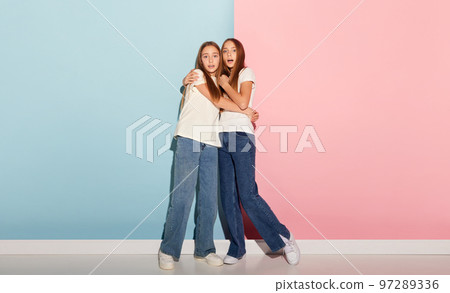 School age girls, sisters friends wearing white t-shirts and jeans communicate isolated over pink-blue background. Concept of love, friendship, family, education, hobbies 97289336