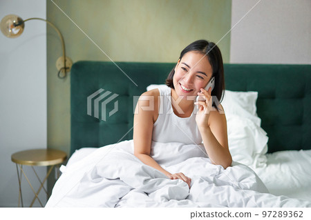 Beautiful young korean woman calling, having a phone call in bed, talking with friend while staying in bedroom Beautiful young korean woman calling, having a phone call in bed, talking with friend while staying in bedroom 97289362