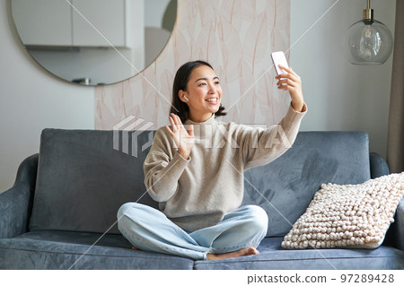 Beautiful chatty girl video chats, making video on smartphone, taking selfie, smiling at mobile phone camera 97289428