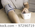 The man is checking blood pressure and heart rate with a digital pressure gauge by herself at home.  97290719