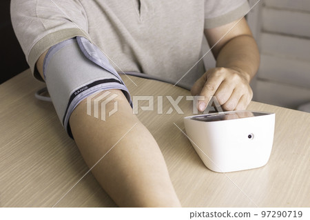 The man is checking blood pressure and heart rate with a digital pressure gauge by herself at home.  97290719