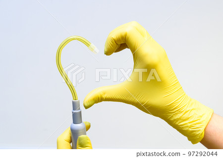 Hand in yellow latex glove and saliva ejector in shape of heart on a white background 97292044