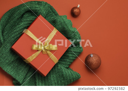 christmas red gift box, golden bow on the red background. Green sweater. New Year concept. Winter holidays and presents. Surprise delivery 97292382