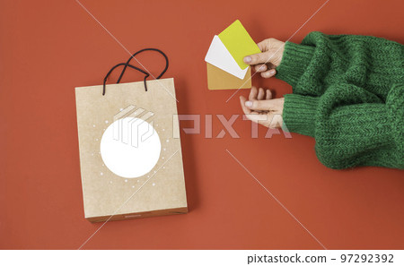 Xmas shopping concept. Woman's hands holding a gift bag and a credit card on a red background, Xmas shopping concept. Woman's hands holding a gift bag and a credit card on a red background, 97292392