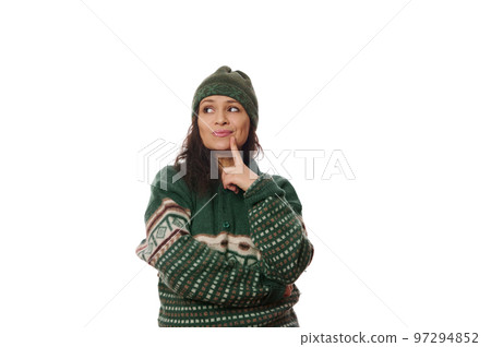 Thoughtful beautiful dark-haired Latin American woman in warm winter knitted lothes, puts her finger on her chin and wistfully looking aside at a copy advertising space on white background 97294852