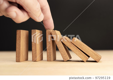 Hand Stopping Falling wooden Dominoes effect Hand Stopping Falling wooden Dominoes effect 97295119