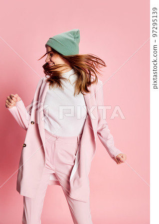 Portrait of young beautiful girl in a suit, hat posing, dancing over pink background. Good mood, positive vibe 97295139