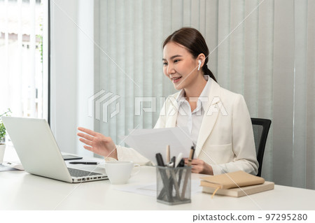 Asian businesswoman talking on the wireless headphones with a colleague in a private office, Telephone communication, Emote conversation, Modern office with laptop and documents on the desk Asian businesswoman talking on the wireless headphones with a colleague in a private office, Telephone communication, Emote conversation, Modern office with laptop and documents on the desk 97295280