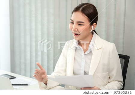 Asian businesswoman talking on the wireless headphones with a colleague in a private office, Telephone communication, Emote conversation, Modern office with laptop and documents on the desk Asian businesswoman talking on the wireless headphones with a colleague in a private office, Telephone communication, Emote conversation, Modern office with laptop and documents on the desk 97295281